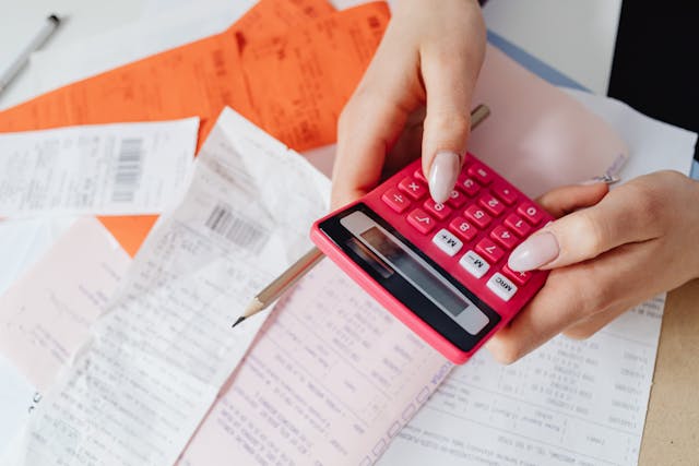 Person holding a calculator and a pencil over top of a pile of receipts